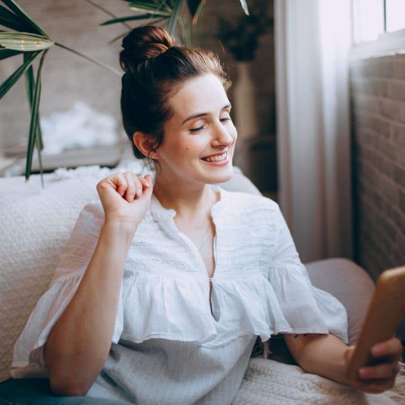 Mujer sonriendo mientras escribe en su teléfono